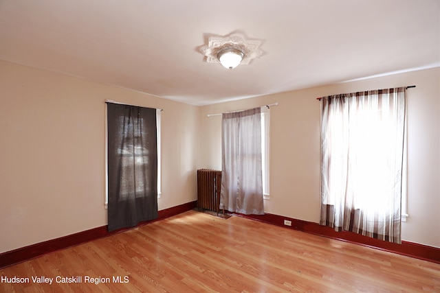 spare room featuring light wood-style flooring, baseboards, and radiator