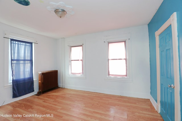 empty room featuring light wood finished floors, baseboards, and radiator