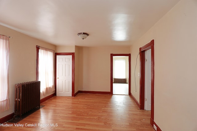 spare room with light wood finished floors, baseboards, radiator, and a healthy amount of sunlight