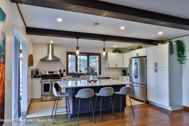 kitchen featuring white cabinetry, wall chimney range hood, appliances with stainless steel finishes, and tasteful backsplash