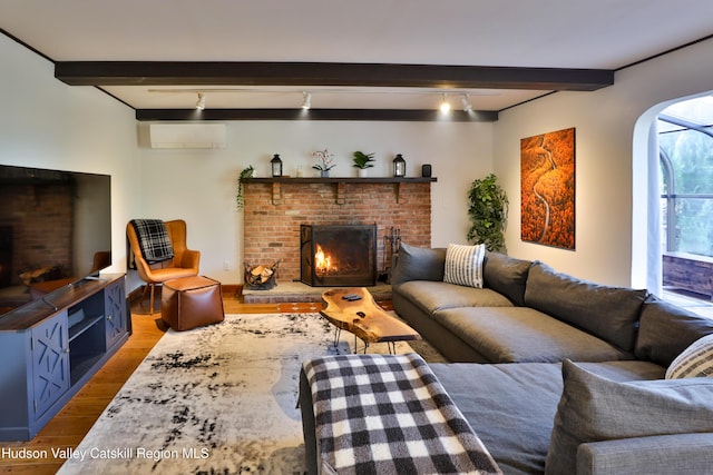 living room featuring beam ceiling, rail lighting, a wall mounted air conditioner, wood-type flooring, and a fireplace