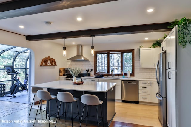 kitchen with stainless steel appliances, white cabinetry, hanging light fixtures, and wall chimney exhaust hood