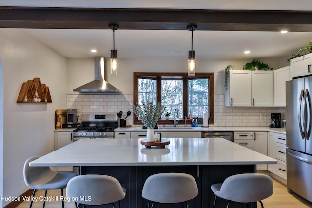 kitchen featuring white cabinets, wall chimney exhaust hood, hanging light fixtures, and appliances with stainless steel finishes