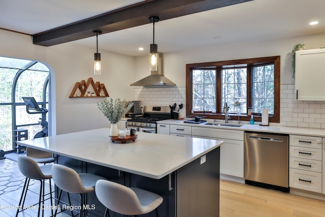 kitchen with decorative backsplash, appliances with stainless steel finishes, white cabinets, a kitchen island, and hanging light fixtures