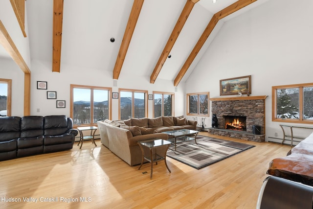 living room with a baseboard heating unit, light hardwood / wood-style flooring, high vaulted ceiling, a mountain view, and a stone fireplace