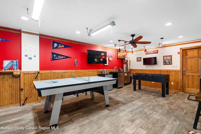 game room featuring hardwood / wood-style floors, wooden walls, ceiling fan, and crown molding