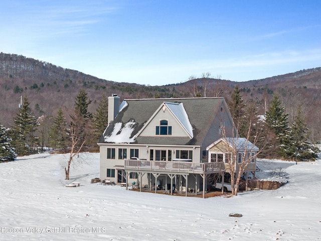 snow covered rear of property featuring a deck with mountain view