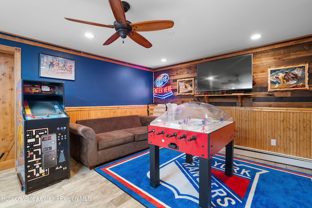 game room with hardwood / wood-style floors, a baseboard heating unit, crown molding, wooden walls, and ceiling fan