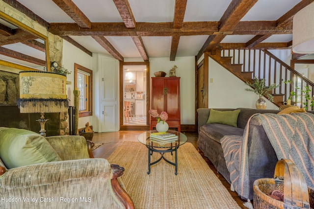 living area featuring beamed ceiling, baseboards, wood finished floors, and stairs
