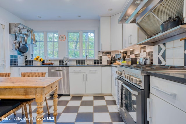 kitchen featuring wall chimney range hood, light floors, decorative backsplash, appliances with stainless steel finishes, and a sink