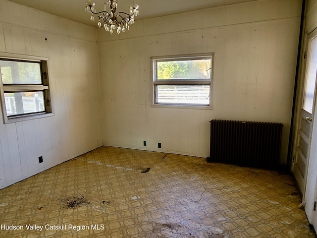 unfurnished room featuring radiator heating unit, wooden walls, and an inviting chandelier