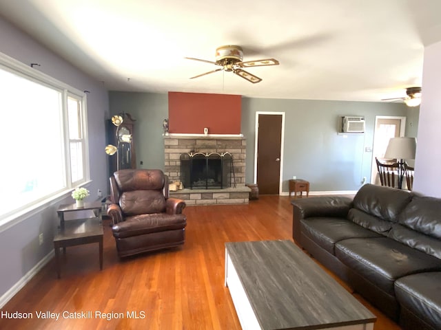 living area with baseboards, a ceiling fan, a wall unit AC, light wood-type flooring, and a fireplace