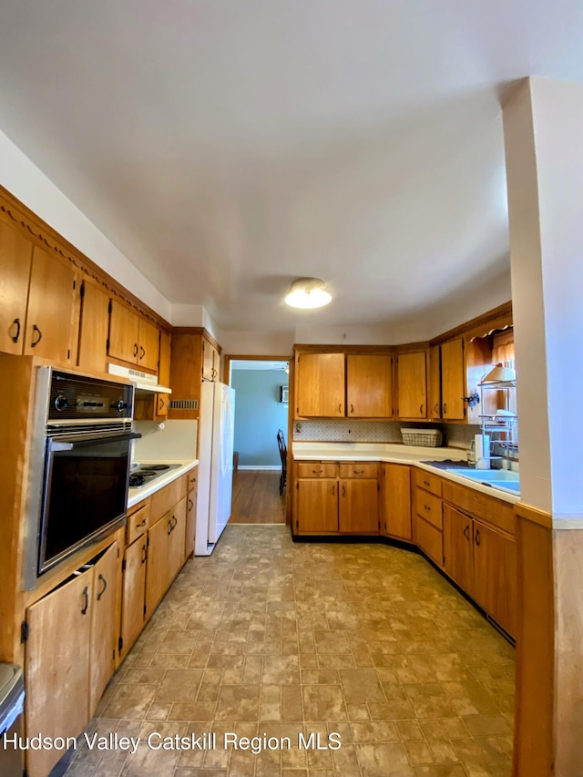 kitchen featuring oven, under cabinet range hood, light countertops, freestanding refrigerator, and brown cabinets