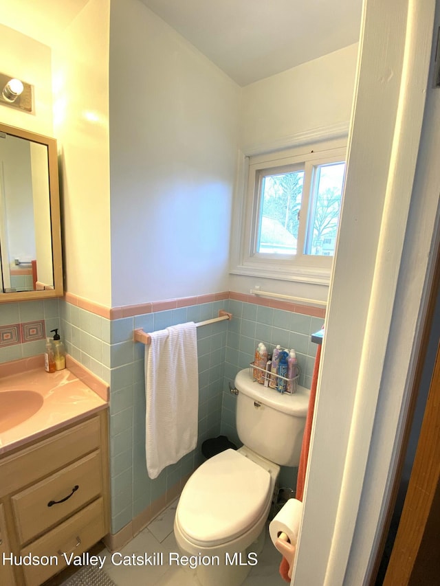 bathroom featuring toilet, a wainscoted wall, tile walls, and vanity