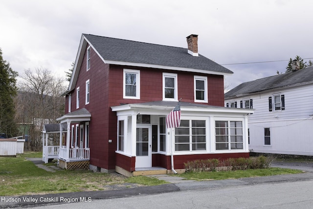 view of front of house with a shingled roof, a chimney, and a sunroom