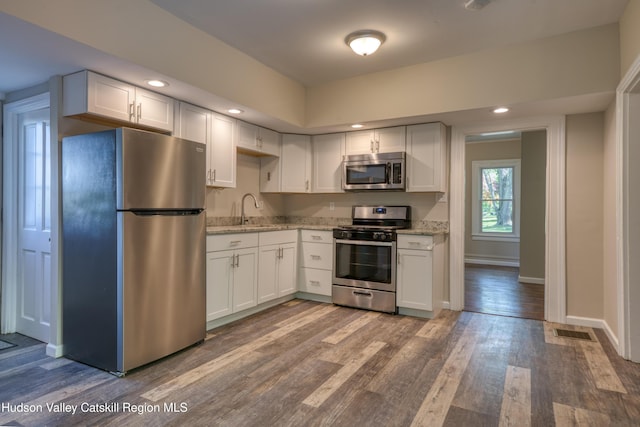 186 2nd St, Port Ewen, NY 12417 - kitchen with appliances with stainless steel finishes, white cabinetry, wood finished floors, light stone countertops, and baseboards