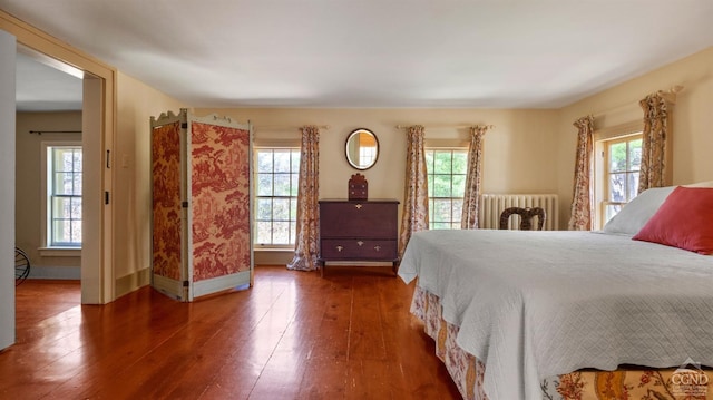 bedroom featuring radiator, multiple windows, wood-type flooring, and baseboards