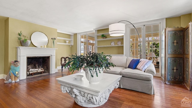 living room featuring wood finished floors, a fireplace with flush hearth, and built in shelves