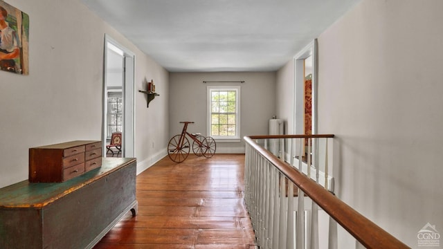 corridor with hardwood / wood-style flooring, radiator heating unit, an upstairs landing, and baseboards