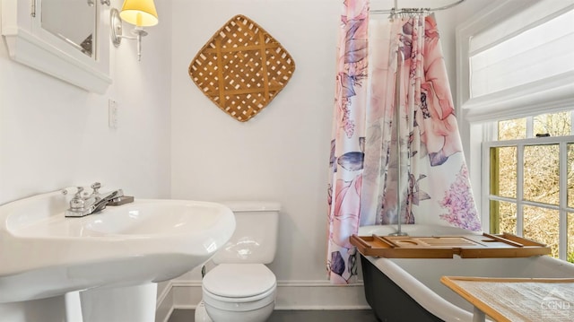 bathroom featuring a soaking tub, toilet, baseboards, a sink, and a shower with curtain