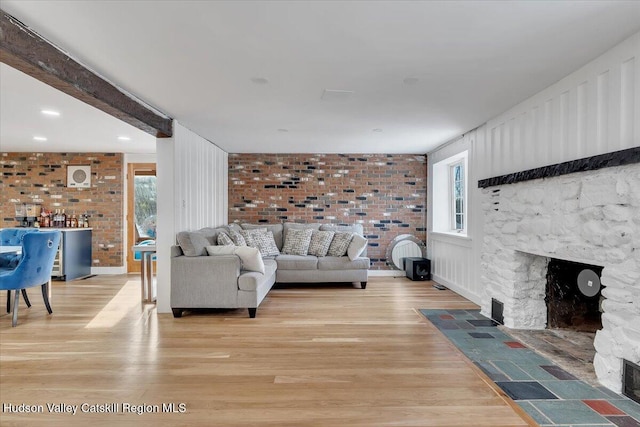 living room featuring beam ceiling, a stone fireplace, light wood-type flooring, and brick wall