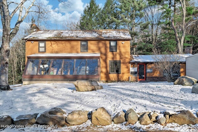 snow covered back of property with a sunroom