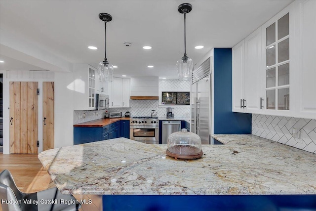 kitchen featuring wooden counters, kitchen peninsula, pendant lighting, white cabinets, and high end appliances