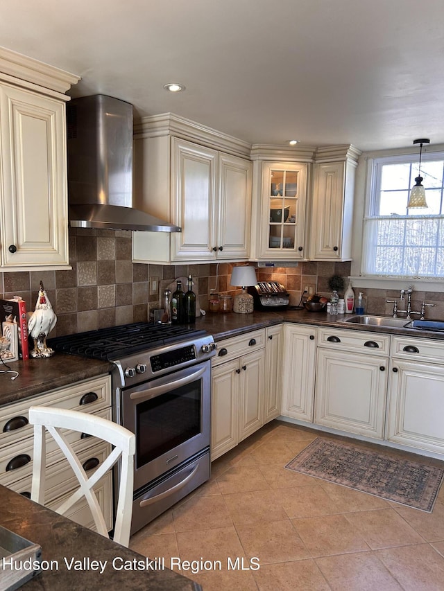 kitchen with gas range, cream cabinets, wall chimney range hood, and a sink