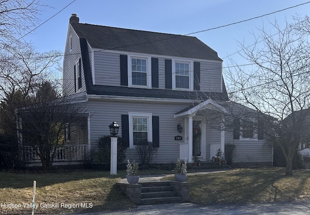 colonial inspired home with a front yard, a gambrel roof, roof with shingles, and a chimney