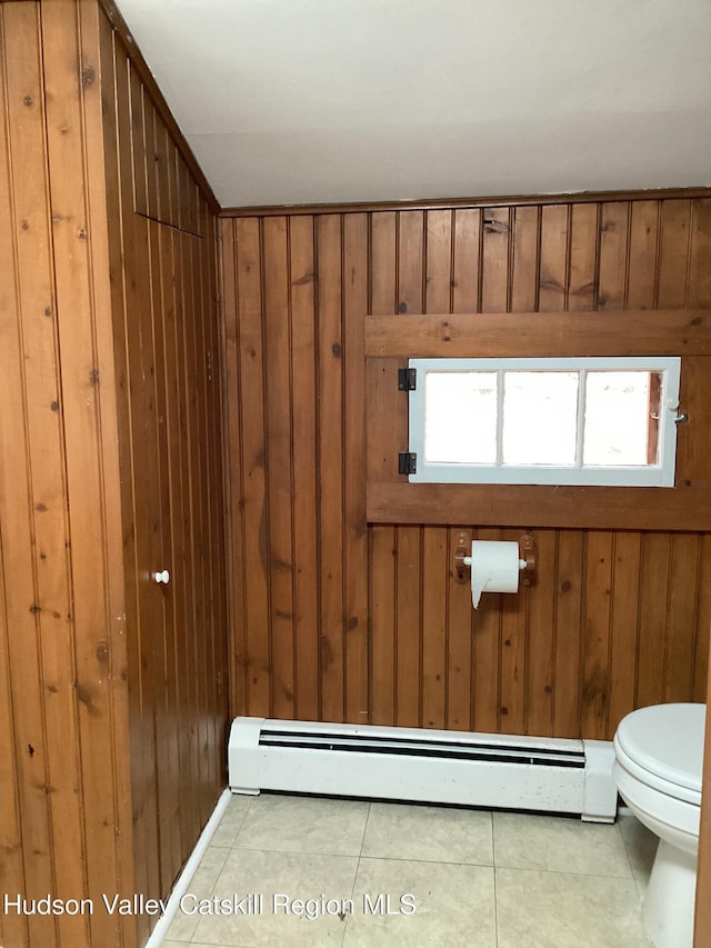 bathroom with tile patterned flooring, a baseboard radiator, wooden walls, and toilet