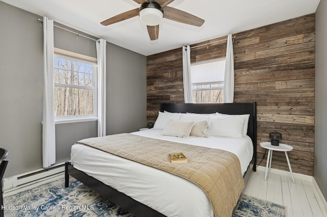bedroom featuring baseboard heating, wood finished floors, wood walls, and a ceiling fan