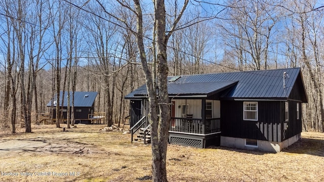 rustic home with a wooded view, a porch, board and batten siding, and metal roof