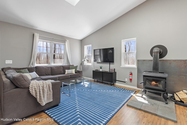 living area featuring a wood stove, baseboards, vaulted ceiling, and wood finished floors