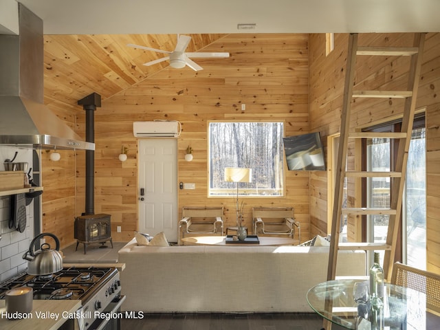 living area with a wall mounted AC, vaulted ceiling, a ceiling fan, wood walls, and a wood stove