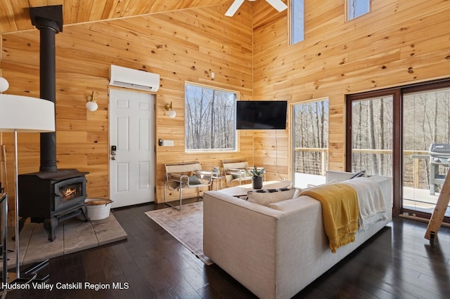 living area featuring a wood stove, ceiling fan, a wall unit AC, wooden walls, and dark wood-style floors