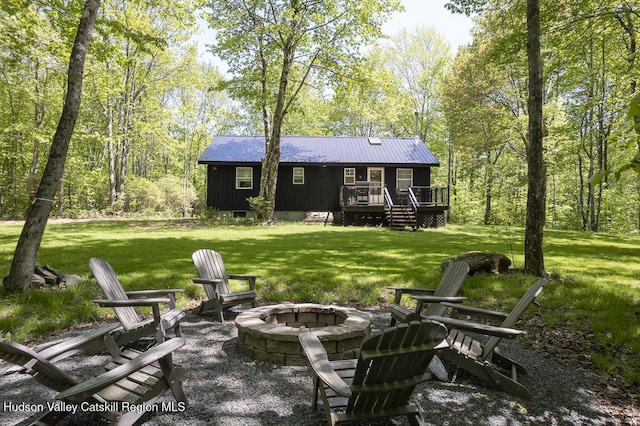 rear view of house with an outdoor fire pit, a wooden deck, metal roof, and a lawn