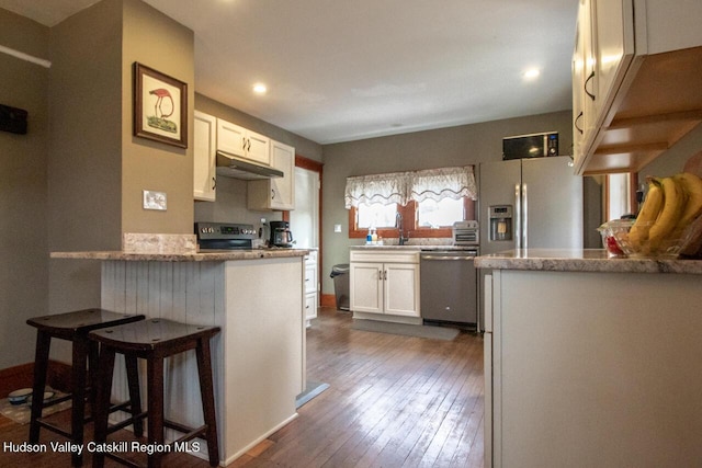 22 Hill St, Napanoch, NY 12458 - kitchen featuring stainless steel appliances, under cabinet range hood, white cabinets, dark wood-style flooring, and a breakfast bar area