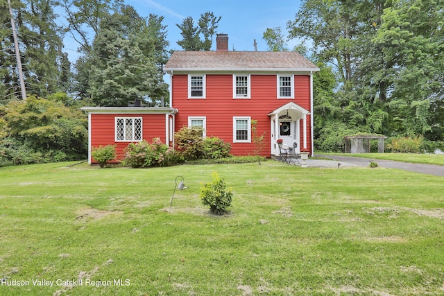 colonial inspired home featuring a chimney and a front lawn