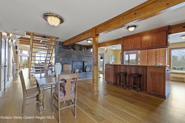 dining space with a fireplace, beamed ceiling, a healthy amount of sunlight, and light hardwood / wood-style flooring