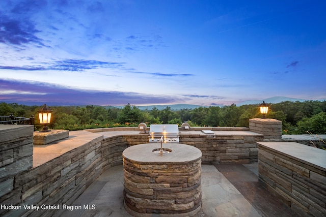 patio terrace at dusk with an outdoor kitchen, a grill, and a mountain view