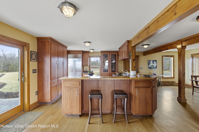 kitchen with kitchen peninsula, light hardwood / wood-style floors, beam ceiling, a kitchen bar, and stainless steel built in refrigerator