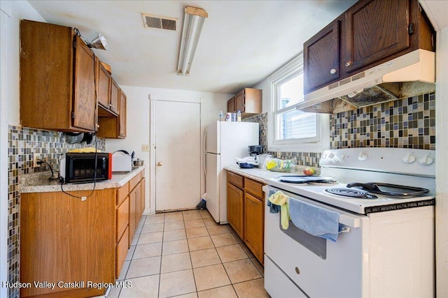 kitchen with light tile patterned flooring, under cabinet range hood, white appliances, visible vents, and light countertops