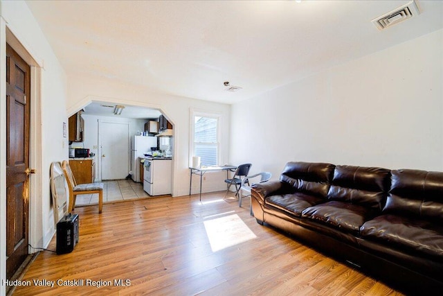 living area with light wood-style floors, visible vents, and arched walkways