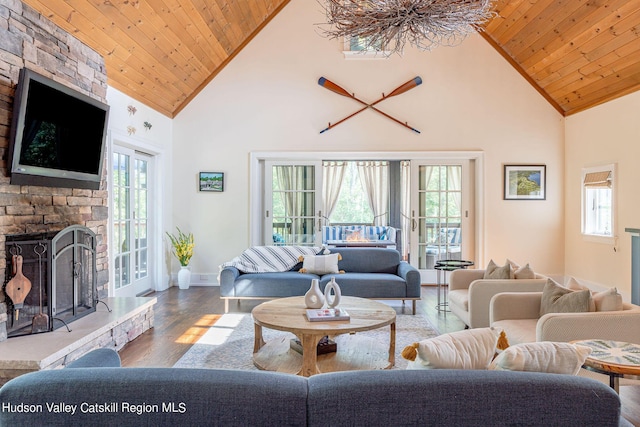 living room featuring wood-type flooring, a stone fireplace, a wealth of natural light, and wooden ceiling