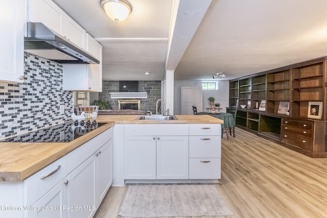 65 Lamb Ave, Saugerties, NY 12477 - kitchen with under cabinet range hood, wood counters, black electric cooktop, a peninsula, and a fireplace