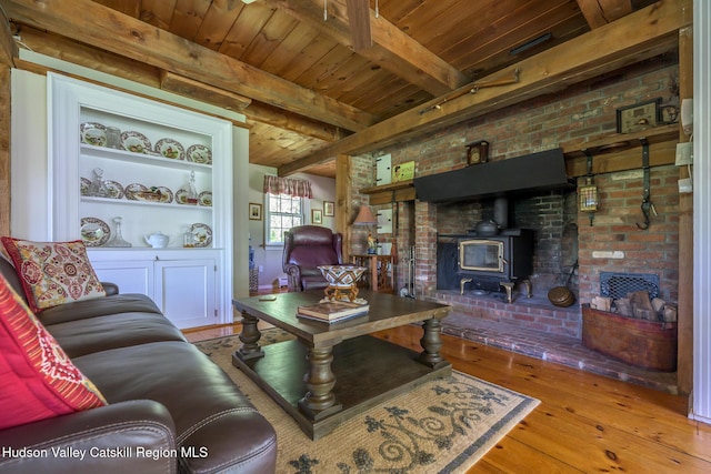 living area with wood-type flooring, a wood stove, wooden ceiling with exposed beams, brick wall, and built in shelves