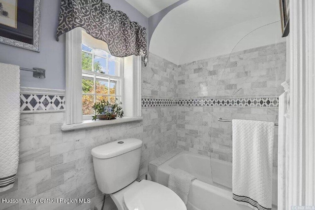 bathroom with tile walls, toilet,  shower combination, and wainscoting