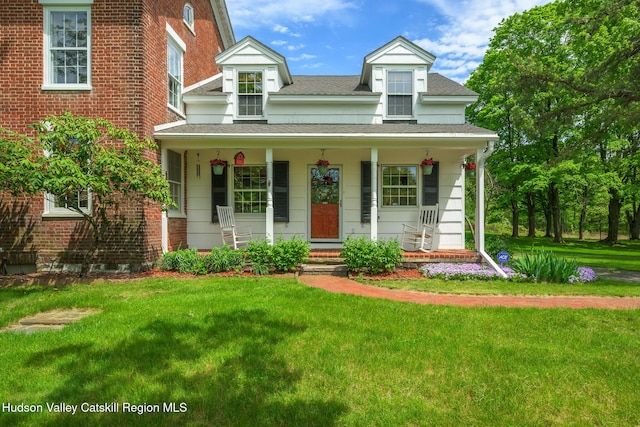 view of front facade with a porch, a front lawn, roof with shingles, and brick siding