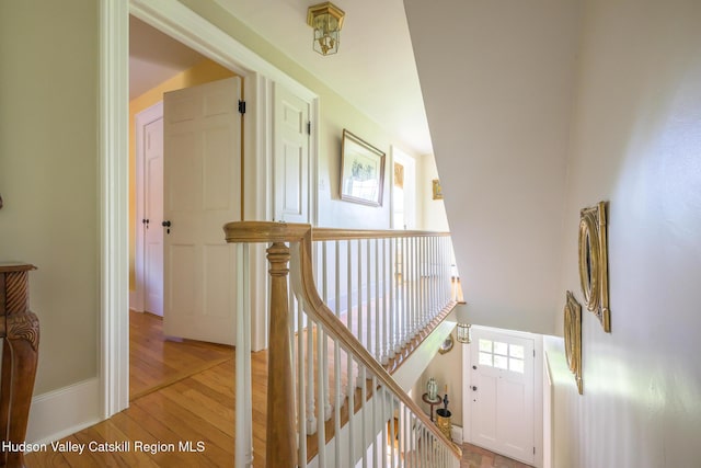 corridor with light wood finished floors, an upstairs landing, and baseboards