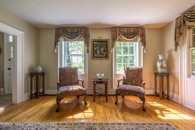 living area with healthy amount of natural light, a baseboard radiator, wood finished floors, and baseboards